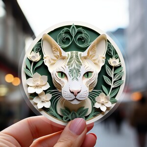 May include: A white paper cut-out of a cat's face with green eyes, surrounded by white paper flowers and green leaves on a green background.