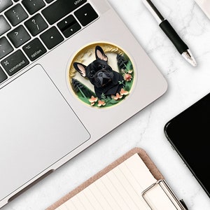 Puede incluir: Un bulldog franc&eacute;s negro con pecho blanco asoma desde una pegatina circular con un dise&ntilde;o floral verde, marr&oacute;n y rosa. La pegatina est&aacute; en un port&aacute;til plateado.