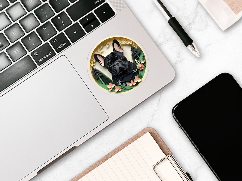 Puede incluir: Un bulldog franc&eacute;s negro con pecho blanco asoma desde una pegatina circular con un dise&ntilde;o floral verde, marr&oacute;n y rosa. La pegatina est&aacute; en un port&aacute;til plateado.