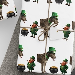 May include: White wrapping paper featuring a repeating pattern of Irish Wolfhounds wearing green top hats, leprechauns with red beards and pipes, and black cauldrons filled with gold coins. The paper is tied with brown twine and star-shaped tags.