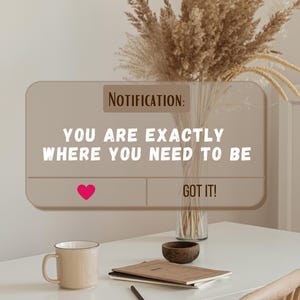 Può includere: Una tazza beige, una ciotola di legno e un taccuino con una penna sono appoggiati su un tavolo bianco. Una grafica di notifica recita "YOU ARE EXACTLY WHERE YOU NEED TO BE" con un cuore rosa e "GOT IT!" sotto. Un vaso di fiori secchi è sullo sfondo.
