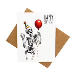 Carte d'anniversaire fêtard - squelette dansant portant un chapeau d'anniversaire et tenant un ballon [Légende : joyeux anniversaire] - livrée avec enveloppe