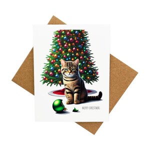 Carte de voeux avec un chat en colère devant un sapin de Noël avec une décoration cassée [Légende : Joyeux Noël] - Livrée avec une enveloppe