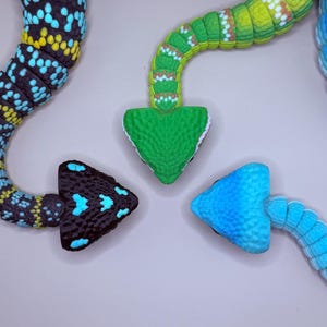 May include: Close-up of three colorful, textured arrow-shaped objects. One is black with turquoise accents, another is green, and the third is blue. The arrows are arranged on a light gray surface.