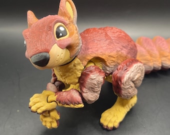May include: A detailed, multi-colored squirrel figurine with a reddish-brown body, yellow paws, and a tan face. The squirrel has large, expressive eyes and a textured appearance, suggesting a 3D-printed or sculpted design. The figurine is posed in a running position.
