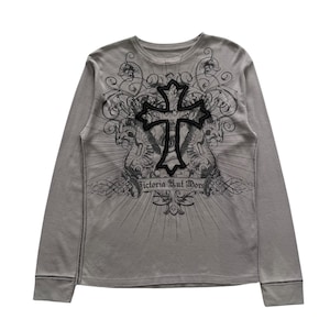 Op de afbeelding: Een grijze longsleeve met een ronde hals. De voorkant van de shirt heeft een groot zwart kruisontwerp, omringd door sierlijke patronen en de tekst "Victoria Hul Mors". De mouwen hebben een gestikte rand.