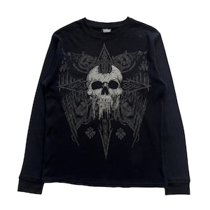 May include: Black long-sleeve thermal shirt with a skull graphic. The skull is gray and white, with a mohawk and dripping details. The graphic is centered on the shirt, with wing and cross designs. The shirt has a crew neck and ribbed cuffs.