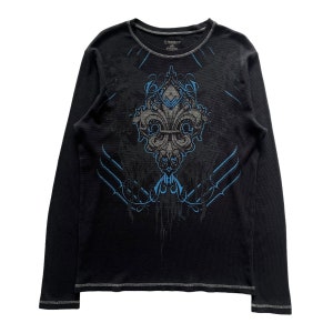 Op de afbeelding: Zwart longsleeve shirt met een blauwe en grijze grafische print van een gestileerde fleur-de-lis.