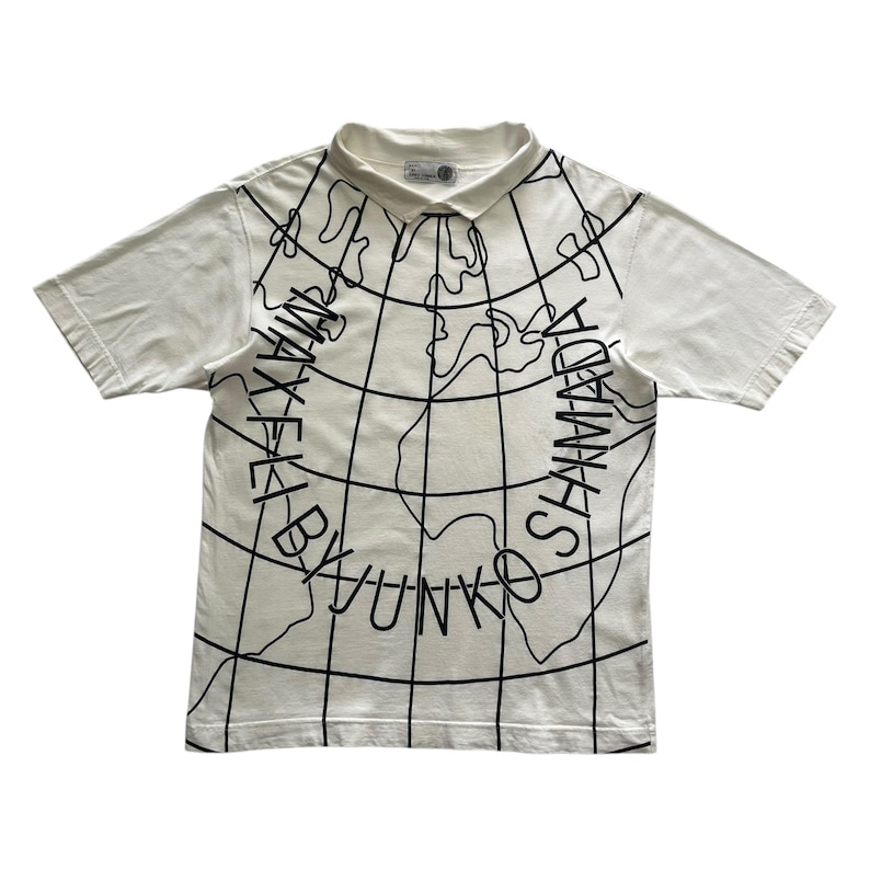 May include: White polo shirt with a black world map design and the text "MAX KEI BY YUNKO SHAMADA" printed on the front. The shirt has short sleeves and a collared neckline.