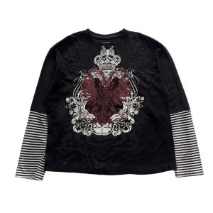 May include: Black long-sleeve shirt with a layered look. The top layer is black with a decorative crest design in burgundy and white. The sleeves have a striped pattern in black and white.