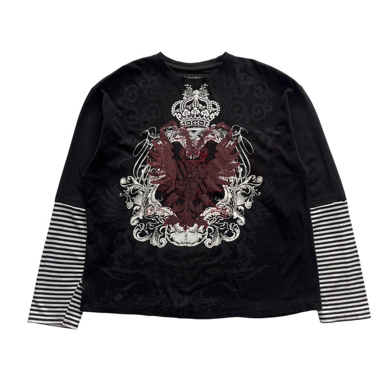 May include: Black long-sleeve shirt with a layered look. The top layer is black with a decorative crest design in burgundy and white. The sleeves have a striped pattern in black and white.