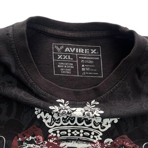 May include: Black XXL cotton t-shirt with a decorative crown design and the brand name AVIREX. The shirt has a crew neck and a tag with washing instructions and fabric details.