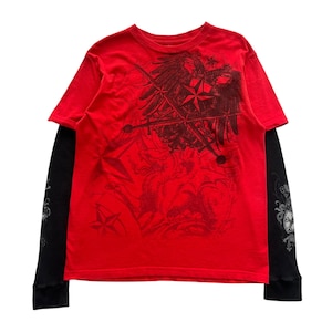 Puede incluir: Camiseta roja con estampado gráfico y camiseta interior negra de manga larga. La camiseta roja presenta un diseño gráfico negro de un águila, estrellas y espadas cruzadas. Las mangas de la camiseta interior negra tienen un patrón texturizado y elementos decorativos.