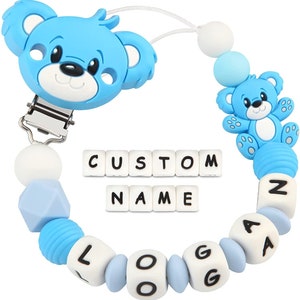 May include: Blue and white silicone baby teether with a bear head clip and beads that spell out the name "Logan". The beads are white with blue accents. The teether also includes a white clip for attaching to clothing.