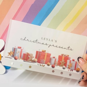 May include: A translucent rectangular planner insert featuring the text LEYLA'S christmas presents in black script and print. The design includes illustrations of red and white gift boxes, gingerbread figures, stars, and ornaments.