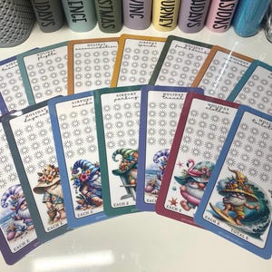 May include: A set of ten colorful printable planner stickers with a gnome theme. Each sticker features a different gnome illustration and a section for tracking activities. The stickers are labeled with titles such as "Holiday Travel", "Holiday Snacks", and "Airport Parking".