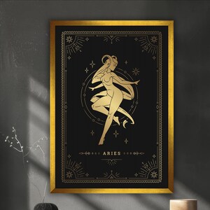 May include: A framed art print featuring a gold illustration of the Aries zodiac sign on a black background. The artwork includes a stylized figure, stars, and decorative borders, all in gold. The frame is gold.