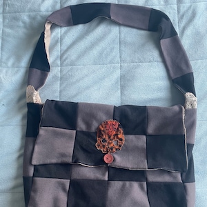 May include: A black and grey patchwork shoulder bag with a skull patch and a red button. The skull patch has the words "Wino Bags" embroidered on it.
