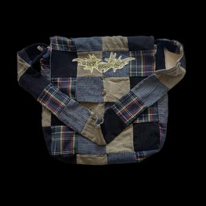 May include: Patchwork shoulder bag in a mix of plaid and denim patches in blue, green, and grey. The bag has a flap closure and a shoulder strap. The text "DIRTY BAGS AC" is embroidered on the front.