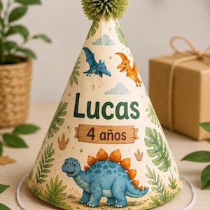 Peut inclure: Un chapeau de fête conique avec un fond crème orné de feuilles tropicales vertes, d'un dinosaure bleu et de ptérosaures volants. Le texte indique Lucas et 4 años sur une plaque en bois. Le chapeau est surmonté d'un pompon vert texturé.