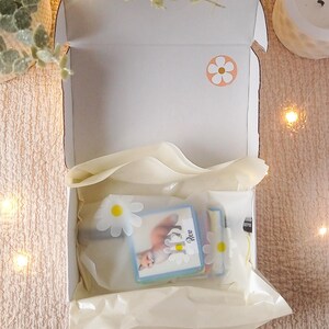 Puede incluir: Una caja de cart&oacute;n blanca con una pegatina de margarita blanca en la parte superior. La caja est&aacute; abierta y contiene una pila de tarjetas de colores con una ilustraci&oacute;n de zorro y la palabra "Rev" en una de las tarjetas. Las tarjetas est&aacute;n envueltas en papel de seda blanco.