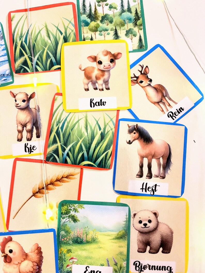 Puede incluir: Cartas de memoria coloridas con im&aacute;genes de animales y escenas de la naturaleza. Las cartas presentan un ternero, un ciervo, una cabra, un caballo, un cachorro de oso, una gallina, trigo y hierba. Las palabras "Kalv", "Rejn", "Kje", "Hest", "Bjornung", "Eng" y "Kje" est&aacute;n escritas en las cartas.