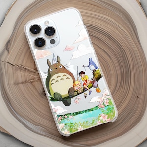 May include: Clear phone case featuring a colorful illustration of characters from a popular animated film. The design includes a large, brown, furry creature with a white belly, and other characters fishing near a river with pink flowers.