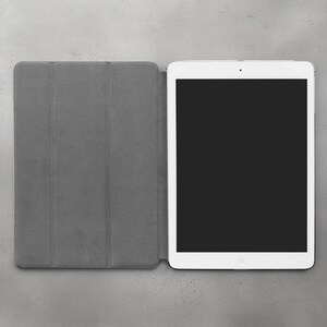 May include: A white tablet computer with a black screen is closed and sitting on a gray surface. The tablet is in a gray case with three sections.