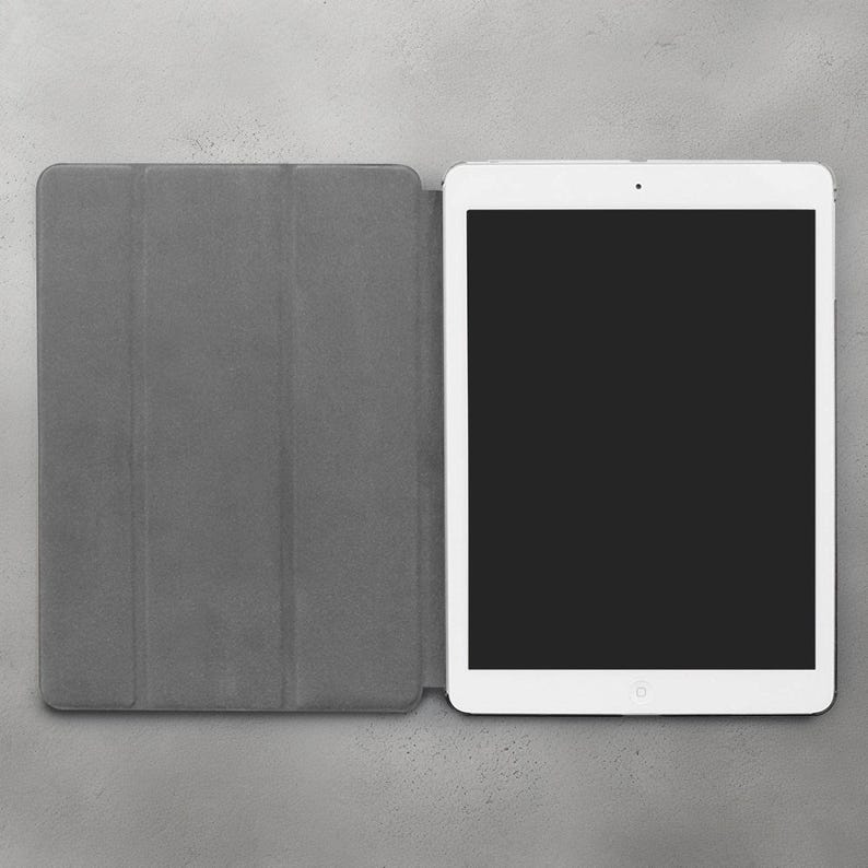 May include: A white tablet computer with a black screen is closed and sitting on a gray surface. The tablet is in a gray case with three sections.