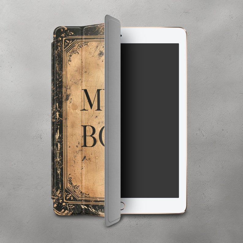 May include: A gray iPad case with a vintage book design. The case has a worn, textured look with the words "My Book" printed on the front.
