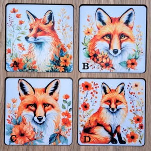 May include: Four square coasters with watercolour fox illustrations. Each coaster displays a different fox pose, framed by orange flowers and foliage. The foxes have orange and white fur with black accents.
