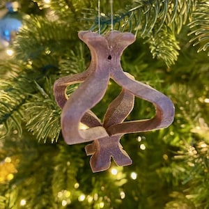 May include: A wooden Christmas ornament shaped like a stylized heart with a hole in the center. The ornament is brown and has a rustic look. It is hanging on a Christmas tree.