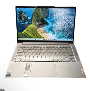 Puede incluir: Un portátil Lenovo plateado con una pantalla de bordes finos que muestra un paisaje costero. El dispositivo cuenta con un teclado QWERTY completo, un panel táctil grande y una pegatina Intel Evo. El logotipo de Lenovo aparece abajo a la derecha.