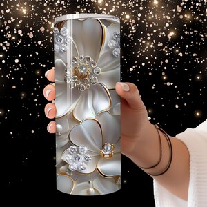 Pu&ograve; includere: Un bicchiere in acciaio inossidabile bianco con un design floreale che presenta fiori bianchi con dettagli dorati e strass scintillanti.