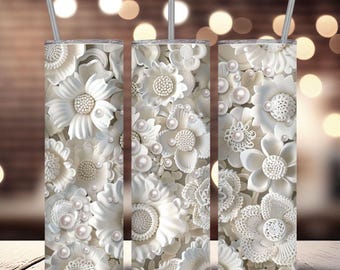 May include: Three white stainless steel tumblers with a floral design featuring white flowers and pearls. The tumblers are all the same design and are arranged in a row.