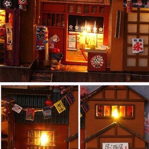K&ouml;nnte beinhalten: Eine Miniatur-japanische Stra&szlig;enszene mit beleuchteten Geb&auml;uden, Schildern und Laternen. Die Szene umfasst ein Ramen-Restaurant und eine Bar mit detaillierten architektonischen Elementen und japanischem Text. Das Farbschema ist warm, mit beleuchteten Innenr&auml;umen.