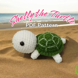 May include: A crocheted turtle toy with a white body and green shell. The toy is sitting on a sandy beach with the ocean in the background. The text "Shelly the Turtle PDF Pattern" is written above the toy.