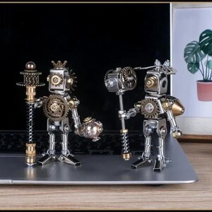 May include: Two steampunk-style robot figurines made of metal and gears. One robot holds a staff, the other a hammer. The robots have intricate details, including cogwheels, and are posed on a laptop.