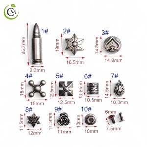 K&ouml;nnte beinhalten: Eine Sammlung silberfarbener Metallnieten und -stifte in verschiedenen Formen, darunter eine Kugel (35,7 mm), ein Stern (19 mm), ein Pik-Symbol (14,8 mm), ein Kreuz (15 mm), ein Puzzleteil (12,5 mm), ein Zylinder (10,5 mm), eine Flamme (14,5 mm), ein Schneeflocke (11,5 mm), eine Rose (11,5 mm) und ein runder Niet (10 mm).