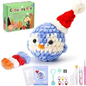 May include: Crochet kit to make a blue penguin plush toy wearing a red Santa hat. The kit includes yarn, a crochet hook, and instructions. The box says "Crochet Kit" and "Including: Step-by-Step Instructions, Accessory Details, Video Tutorials".