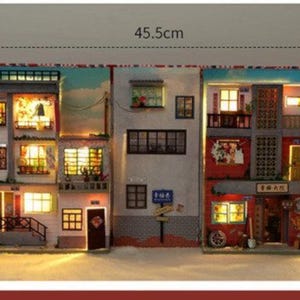 May include: A miniature dollhouse model of a three-storey building with a street scene. The building has a red roof, white walls, and windows with lights. The street scene includes a lamppost, a sign that says "下楼", and a small tree. The model is 45.5 cm wide.