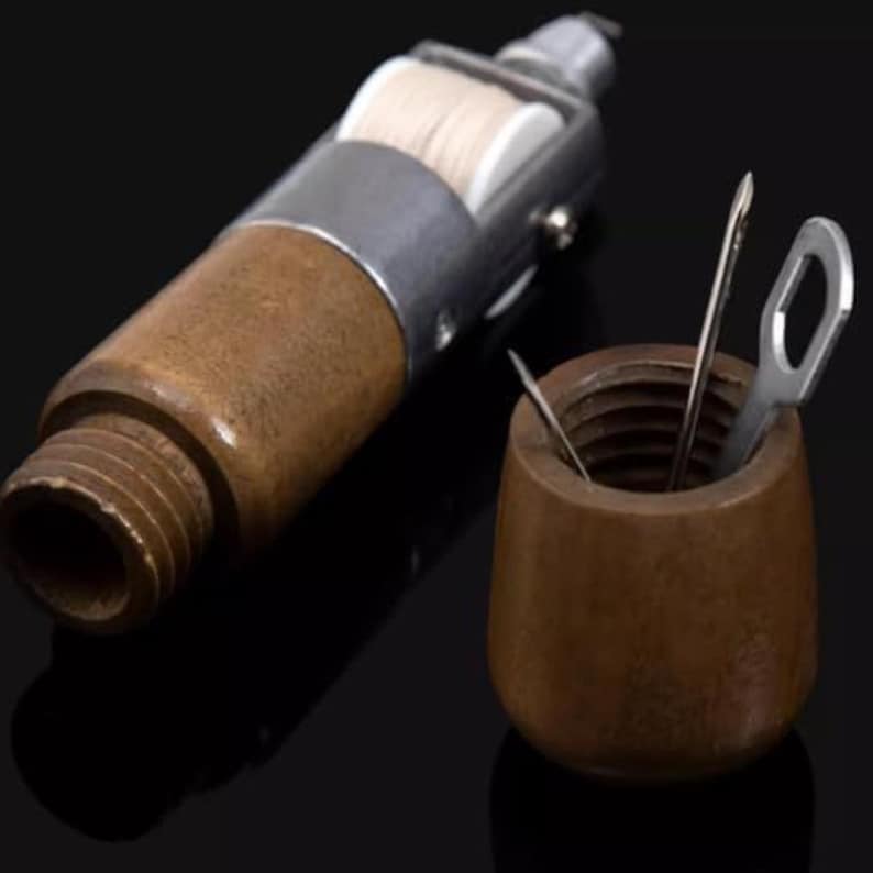 Puede incluir: Una lezna de costura de madera vintage con una bobina de hilo de metal y un peque&ntilde;o recipiente de madera que contiene agujas y una herramienta de metal. La lezna tiene una base roscada y una parte superior de metal.