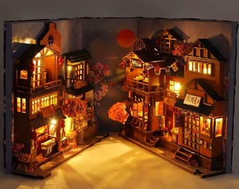 May include: A detailed miniature Japanese village diorama, illuminated within an open book. The wooden structures have warm interior lighting, a red sun, and cherry blossom accents. The scene creates a cosy, inviting atmosphere.