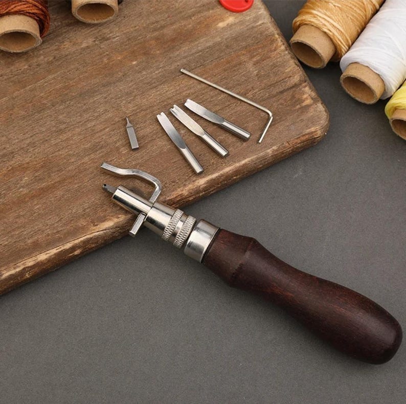 May include: A leather stitching tool with a wooden handle and a set of interchangeable stitching awls. The awls are made of metal and have different sizes and shapes. The tool is used for stitching leather together.