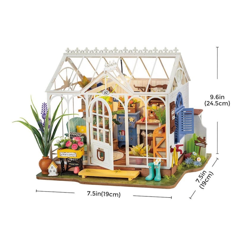 May include: A miniature white greenhouse with a glass roof and open door, showcasing a detailed interior. The model includes miniature furniture, plants, and accessories. The dimensions are 7.5 inches (19 cm) wide and 9.6 inches (24.5 cm) tall.