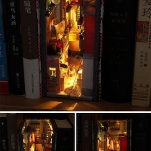 May include: A miniature cityscape built inside a book. The cityscape is lit up with small lights and features a narrow street with buildings on either side. The book is on a bookshelf with other books.