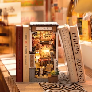 May include: A miniature Japanese street scene diorama with a detailed facade, lit interior, and the text "ふくろ町". The diorama is flanked by three books, including "PHILIPS KONINCI" and "Namiya General Store".