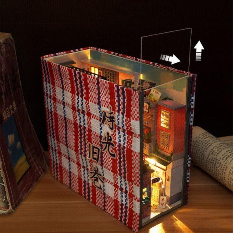 May include: A miniature dollhouse built inside a book with a red and white checked cover. The book is titled "时光旧梦" in Chinese characters. The dollhouse features a lit interior with multiple rooms and windows.