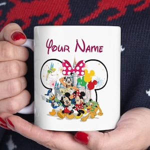 May include: White ceramic mug featuring a Disney character design with Mickey and Minnie Mouse, Donald Duck, and Goofy. The mug has the text "Your Name" in a burgundy script. The design includes a pink bow and colorful balloons.