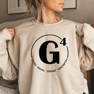 May include: A beige sweatshirt with a black circle graphic. The graphic features a large black "G" with a superscript "4" and the words "GOD", "GOAL", "GRIND", and "GROWTH" around the circle.
